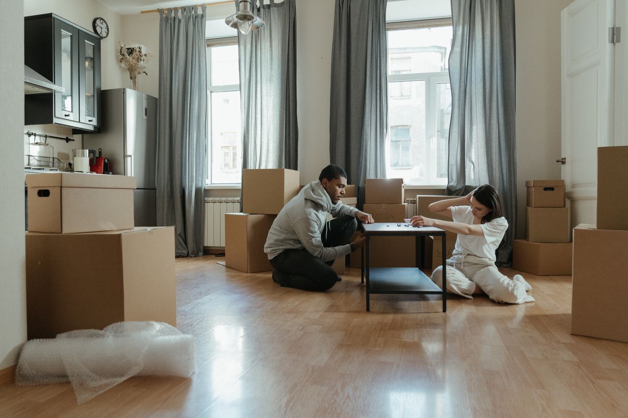 Jeune couple montant des meubles dans leur nouvel appartement, entouré de cartons.
